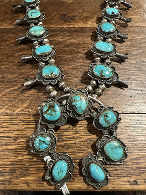 Sterling silver squash blossom necklace with chocolate matrix veined natural Bisbee turquoise, displayed against a wooden background.