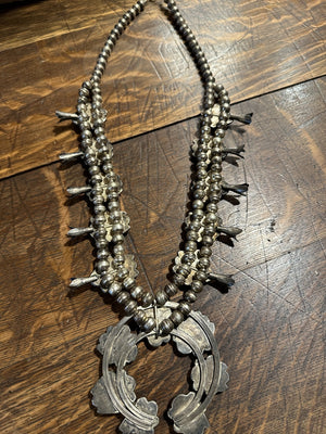 Sterling silver squash blossom necklace with chocolate matrix veined natural Bisbee turquoise, displayed against a wooden background.