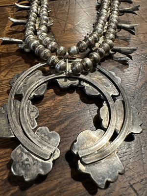 Sterling silver squash blossom necklace with chocolate matrix veined natural Bisbee turquoise, displayed against a wooden background.