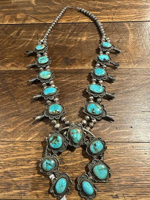 Sterling silver squash blossom necklace with chocolate matrix veined natural Bisbee turquoise, displayed against a wooden background.