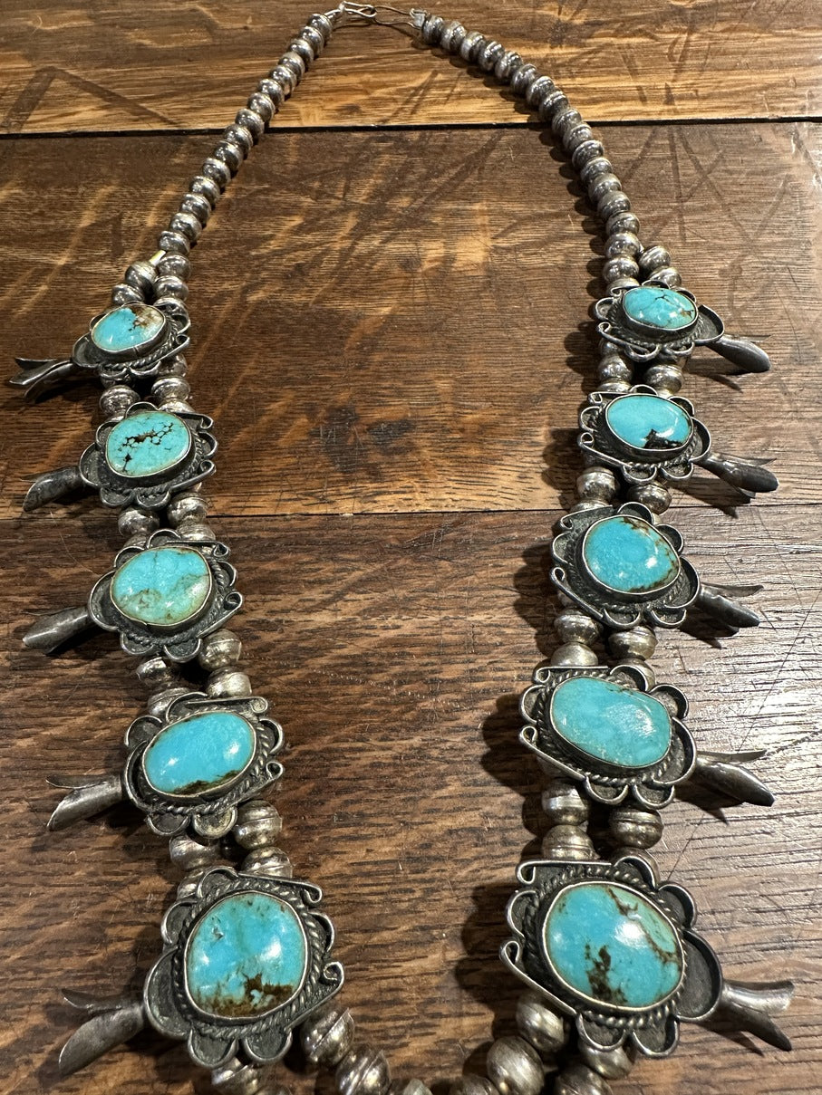 Sterling silver squash blossom necklace with chocolate matrix veined natural Bisbee turquoise, displayed against a wooden background.
